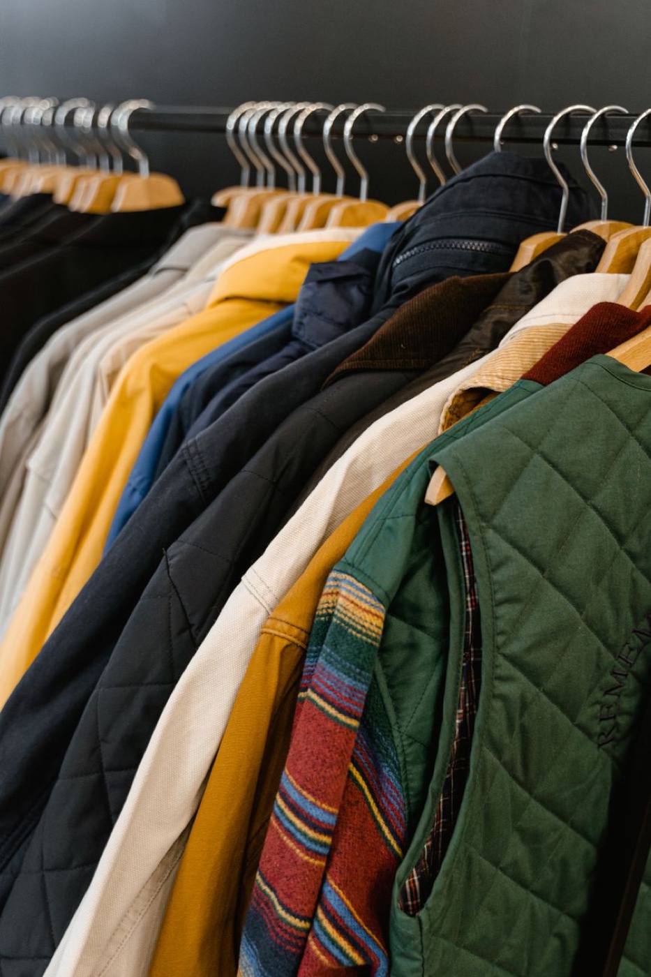 A row of jackets and a quilted vest hanging on wooden hangers on a store rack