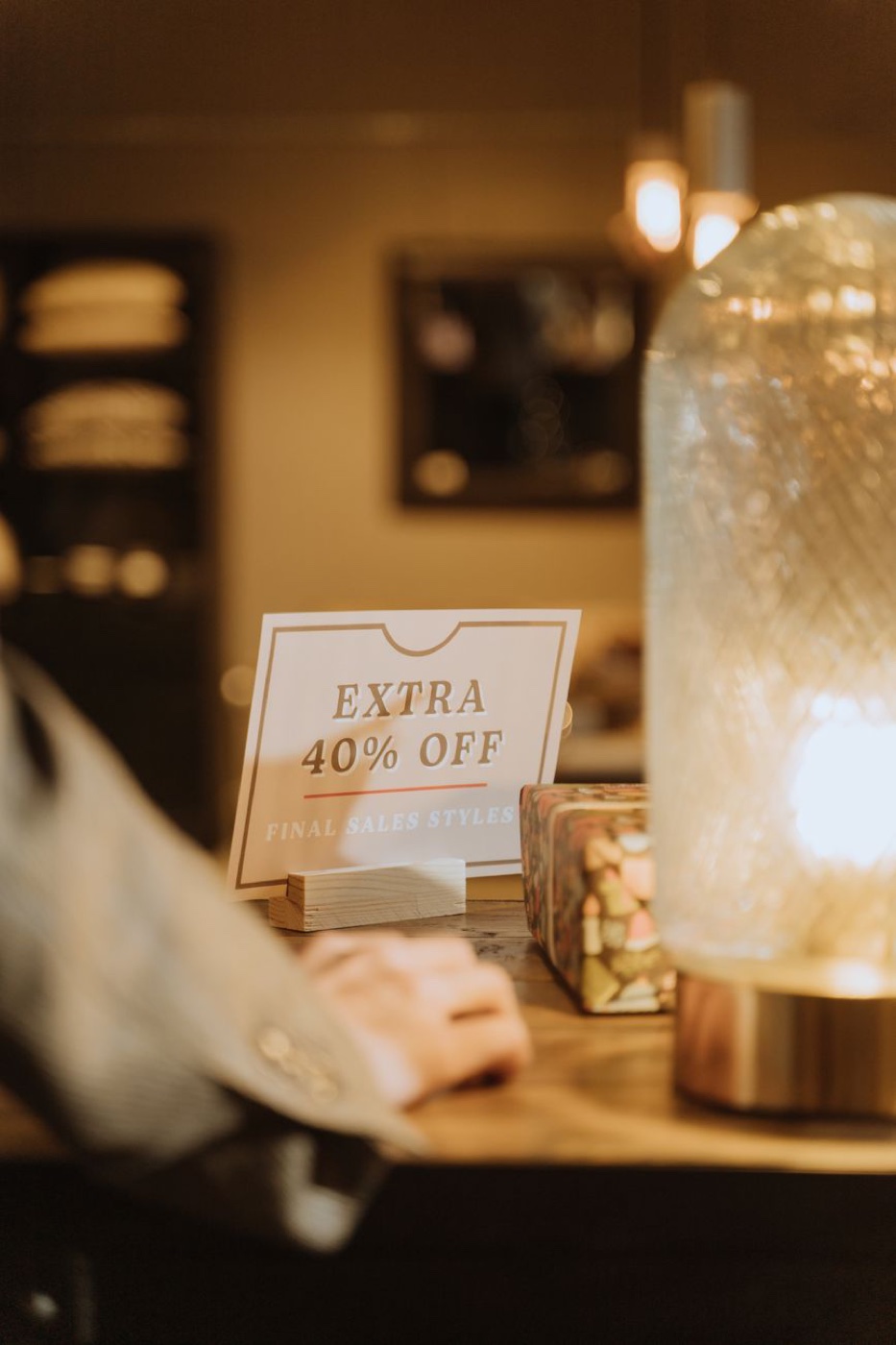 A printed card on a wooden stand in a warmly lit shop reading Extra 40 percent off, final sales styles
