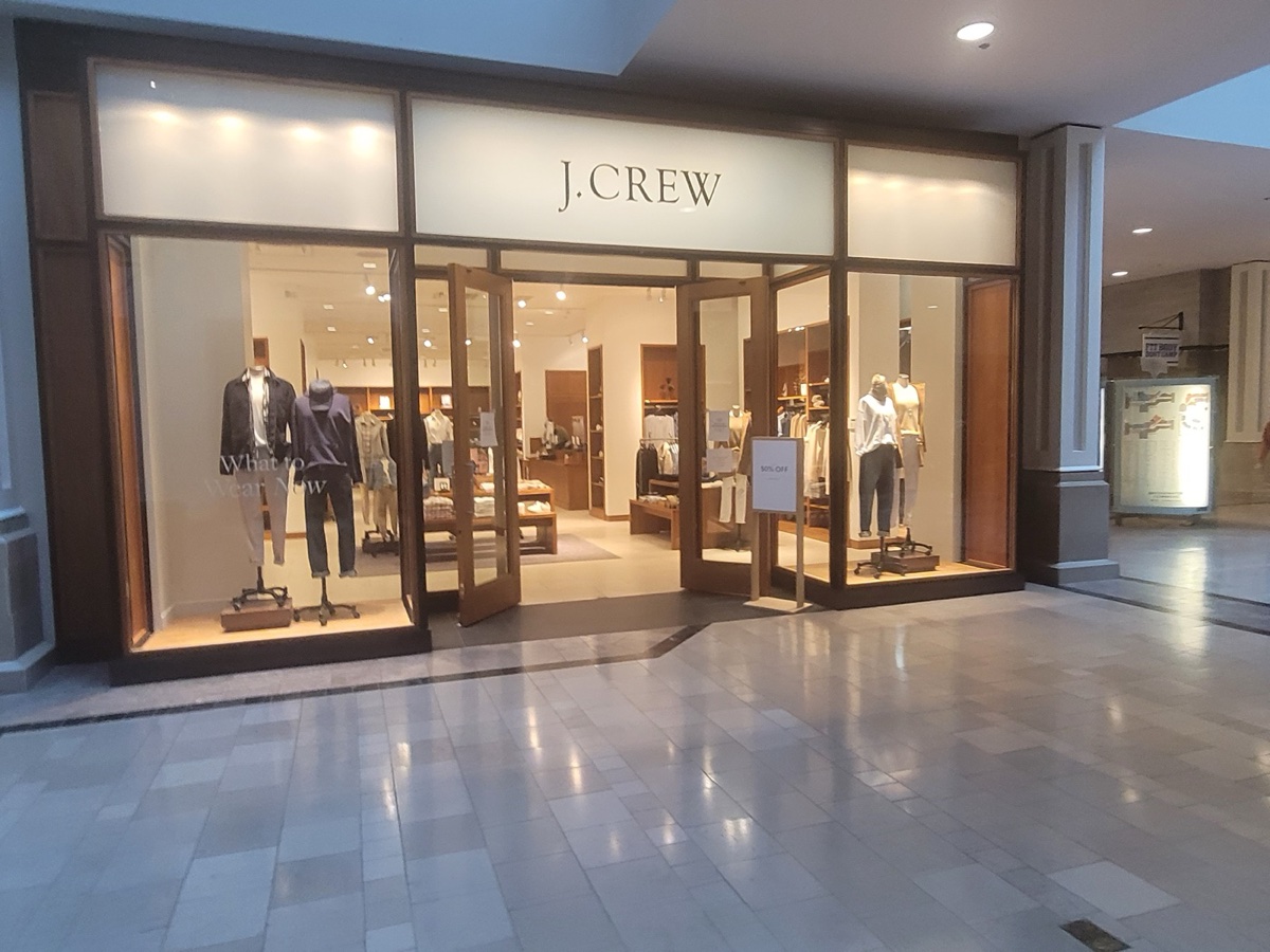 A J.Crew mall storefront with open doors, mannequins in the window, and a 50% off sign visible inside