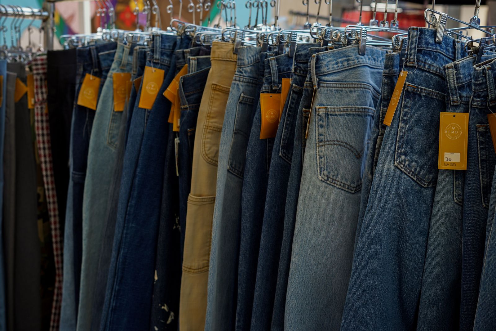 Rows of secondhand jeans hanging on a rack, orange hangtags attached, one white ticket hand-marked 30 with W:30 written beneath