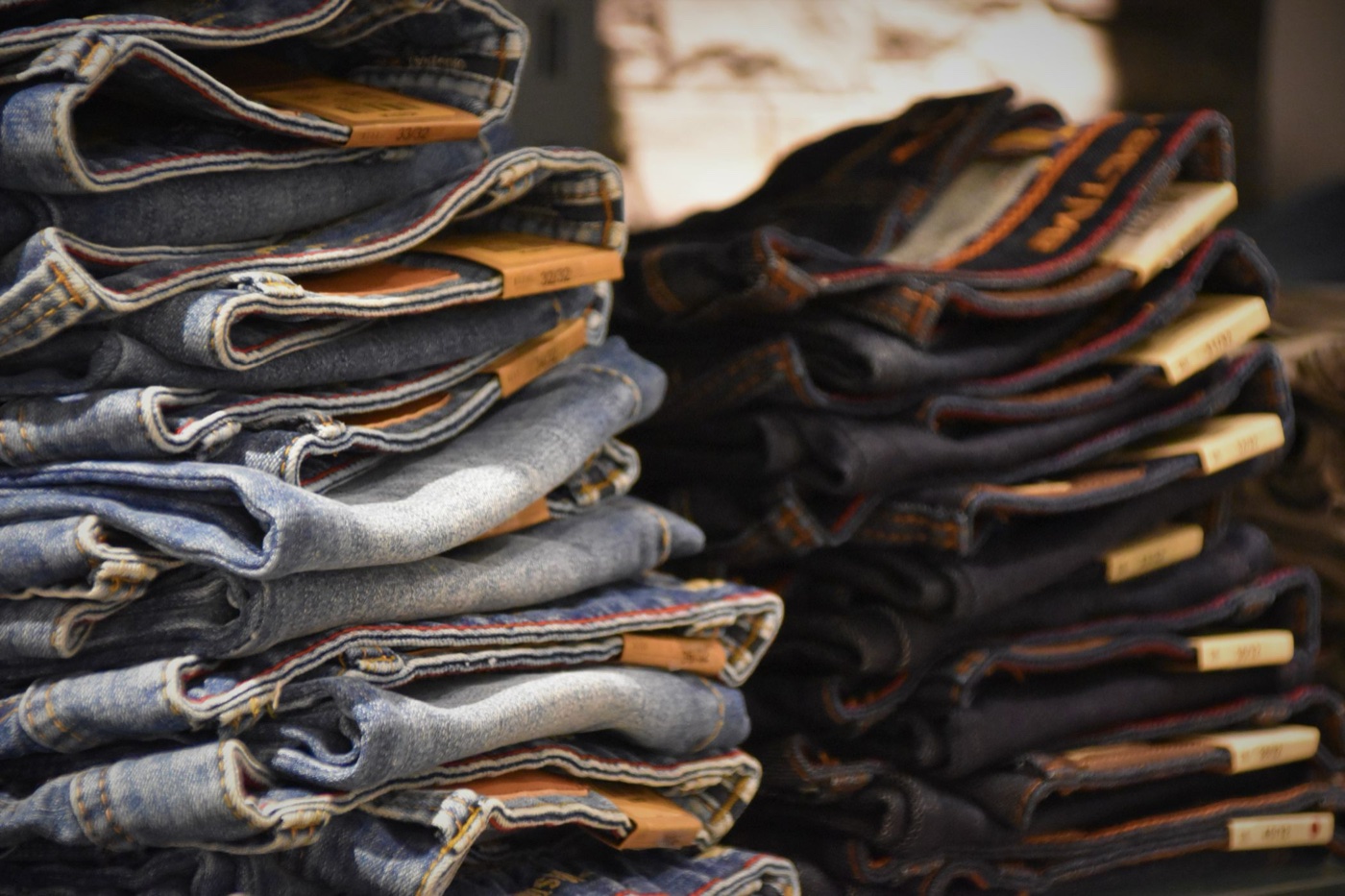 Two tall folded stacks of jeans in a shop, light washes on the left and dark on the right, with cardboard size tags reading 33/32 and 32/32 poking out