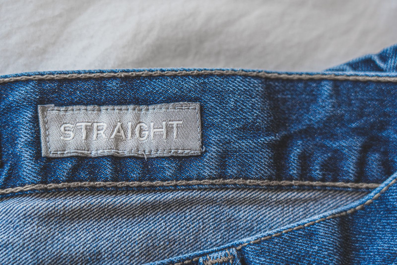 Close-up of a grey woven label reading STRAIGHT stitched to the waistband of blue jeans