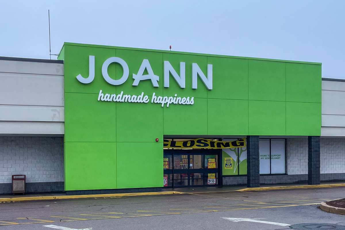 Joann fabrics storefront with green facade and yellow store closing banners over the entrance on an overcast day