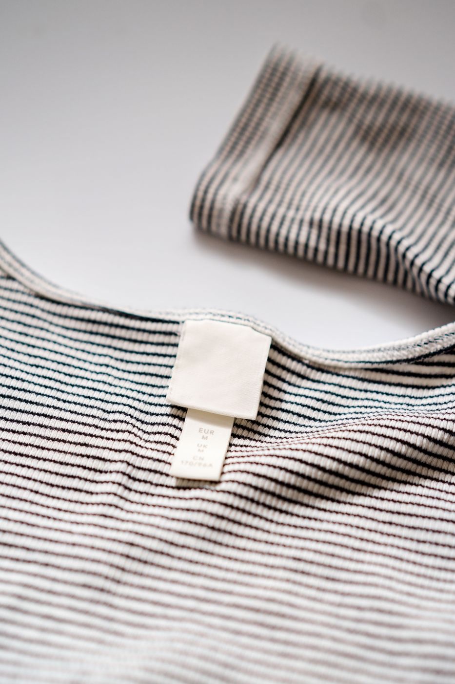 A striped rib-knit top laid flat with a blank white brand label and a size tab reading EUR M, UK M