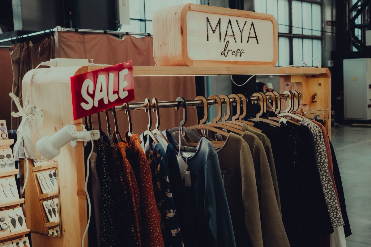 A wooden rack of printed dresses and blouses in a small boutique, a red SALE tag hung on the end of the rail