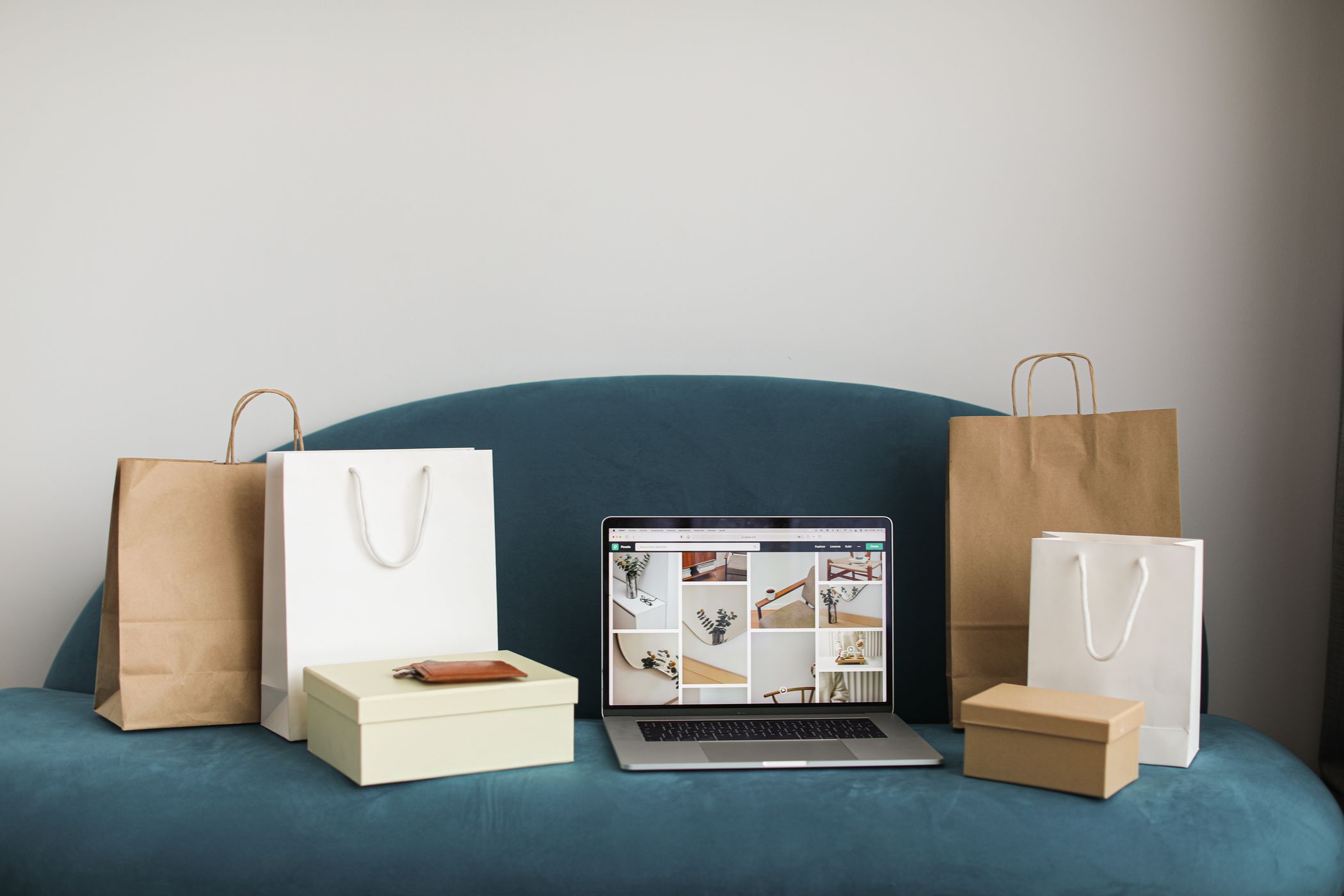 An open laptop on a blue sofa surrounded by paper shopping bags and boxes