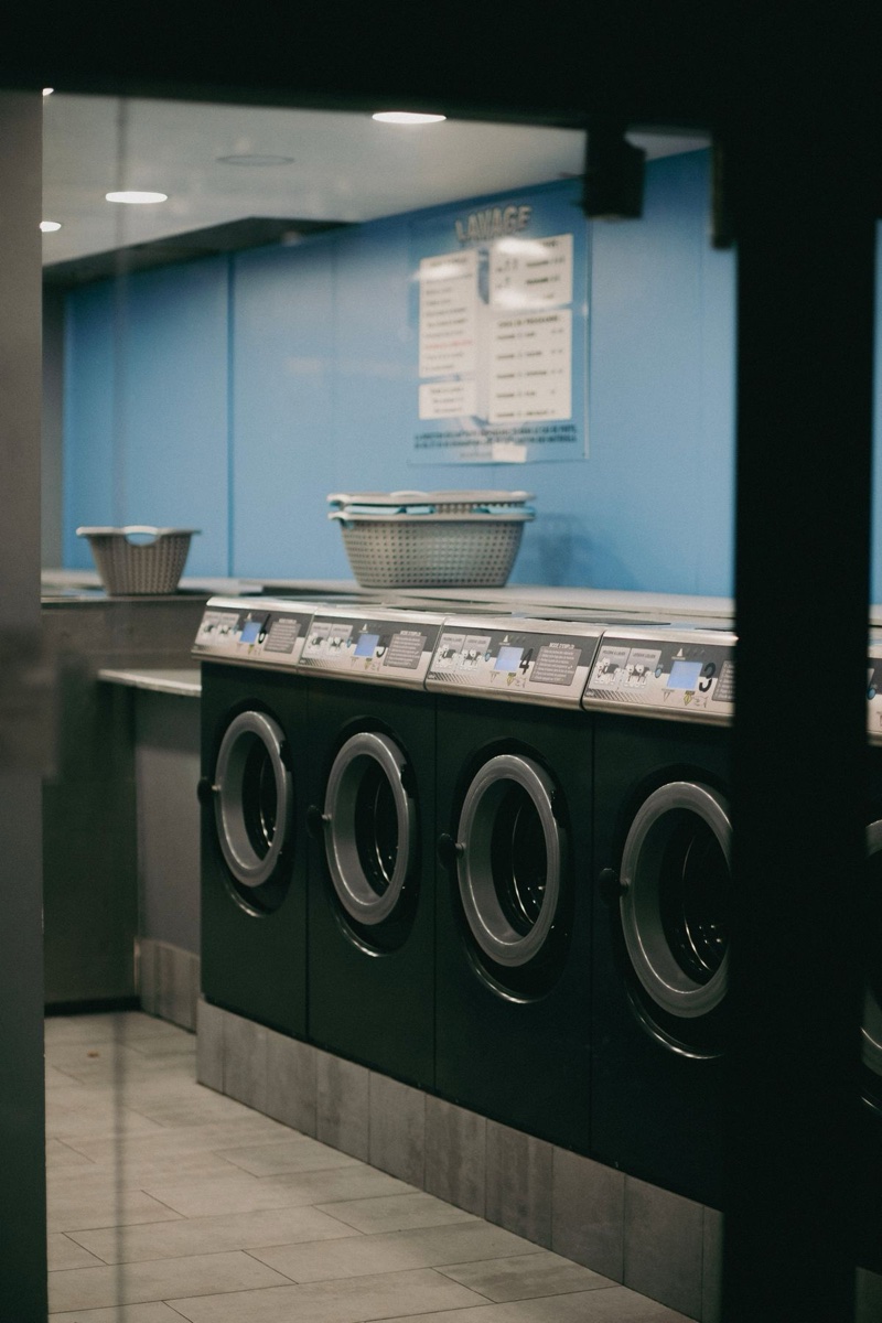 A Paris laundromat seen through its doorway, front-loading machines in a row and a printed price list posted on the blue wall
