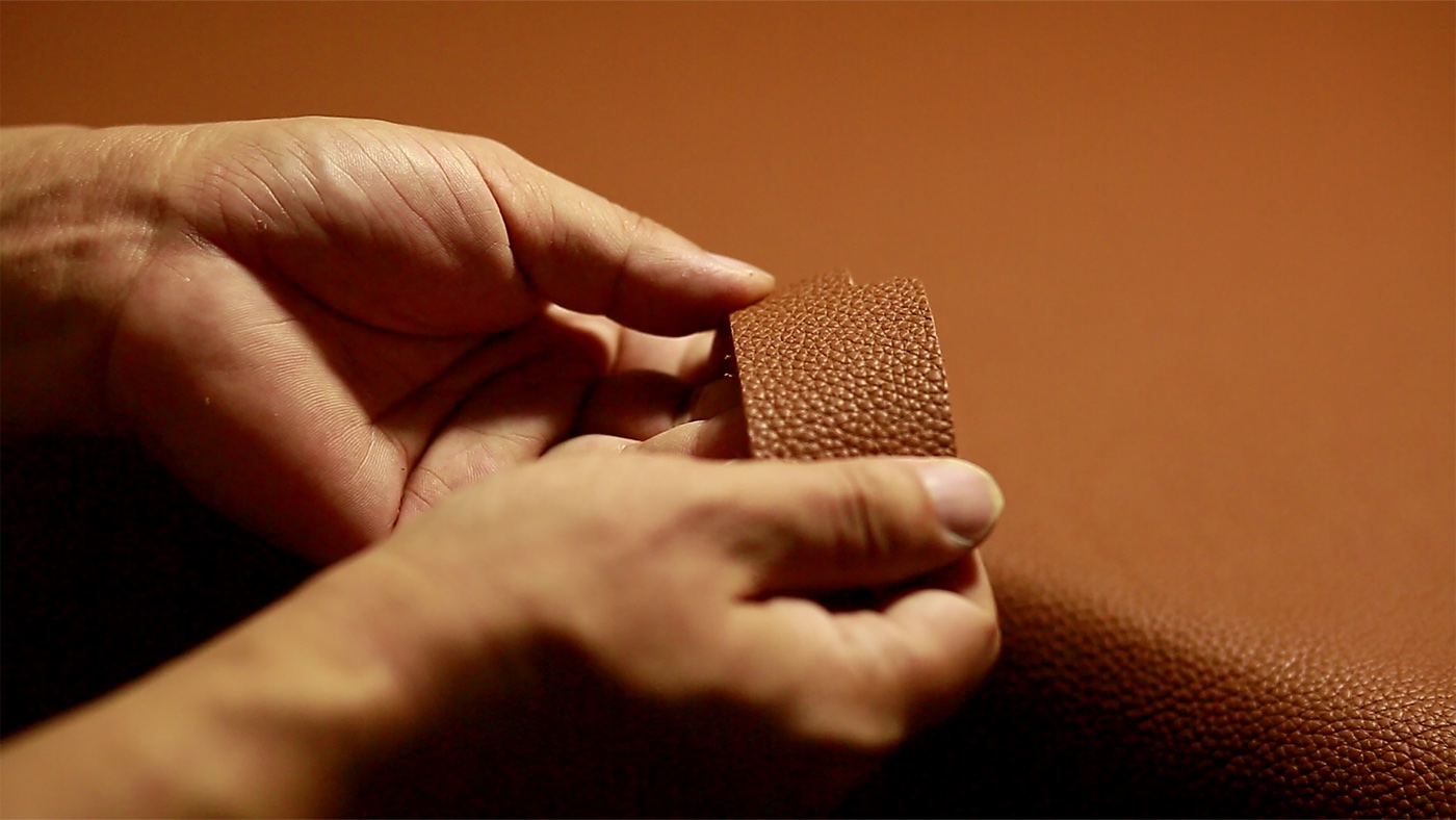 Close-up of hands bending a small strip of pebbled brown leather above a larger leather hide