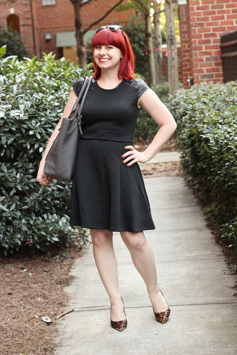 An outfit with a black textured dress, gray work tote, and leopard print pointed-toe heels on a garden path