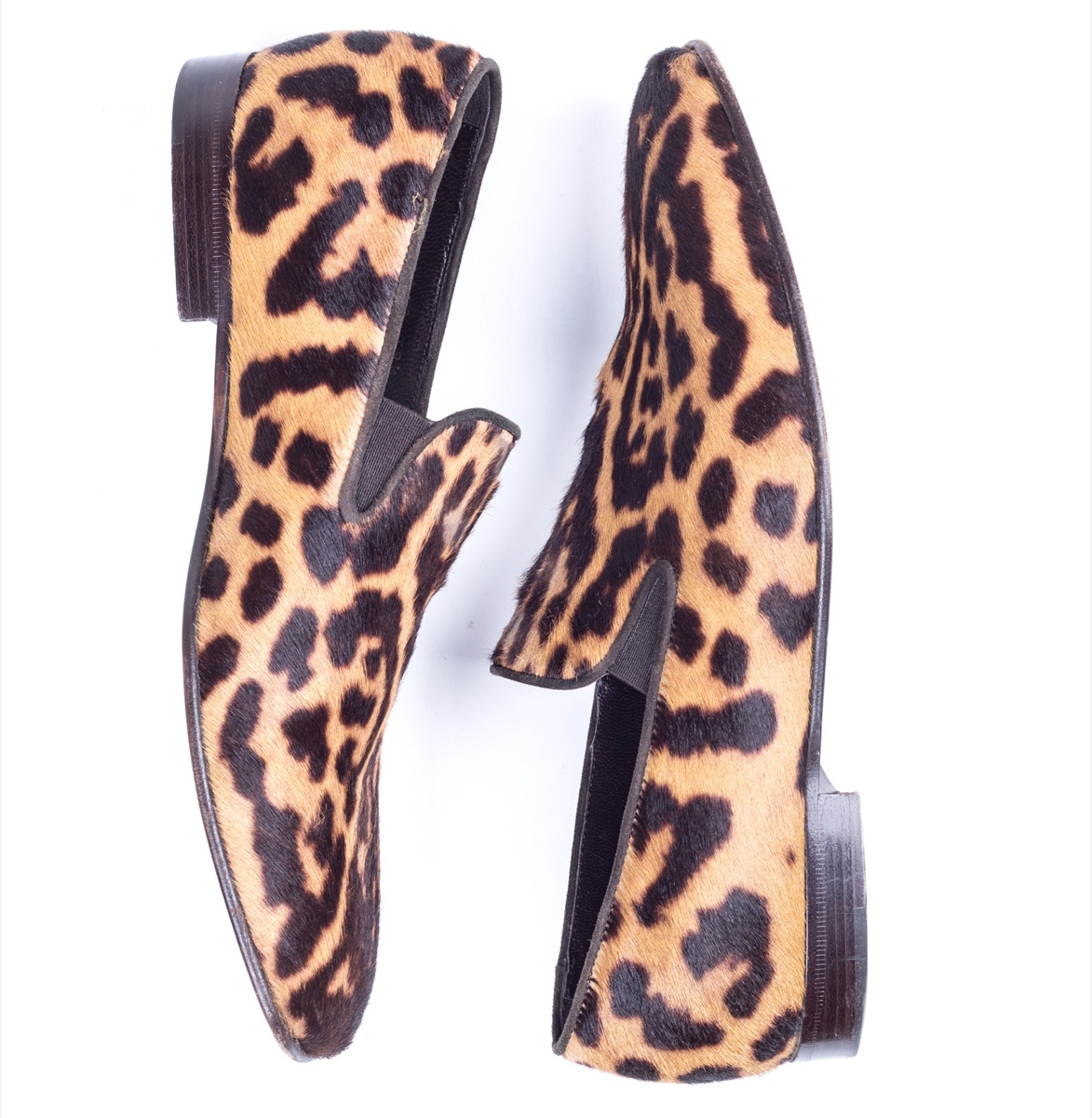 A pair of Yves Saint Laurent leopard print pony-hair loafers with dark stacked heels, laid sole to sole on a white background