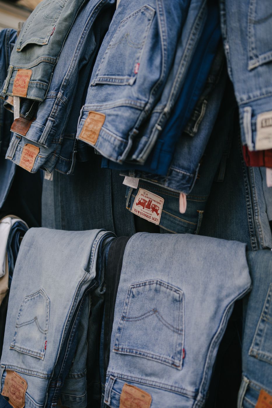 Folded and hanging blue jeans layered on a display in a clothing store, leather patch labels visible on several waistbands