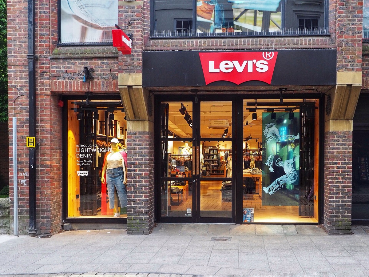 Brick-fronted Levi's shop in York in May, a window decal reading Introducing Lightweight Denim beside a mannequin in a denim skirt, no sale signage