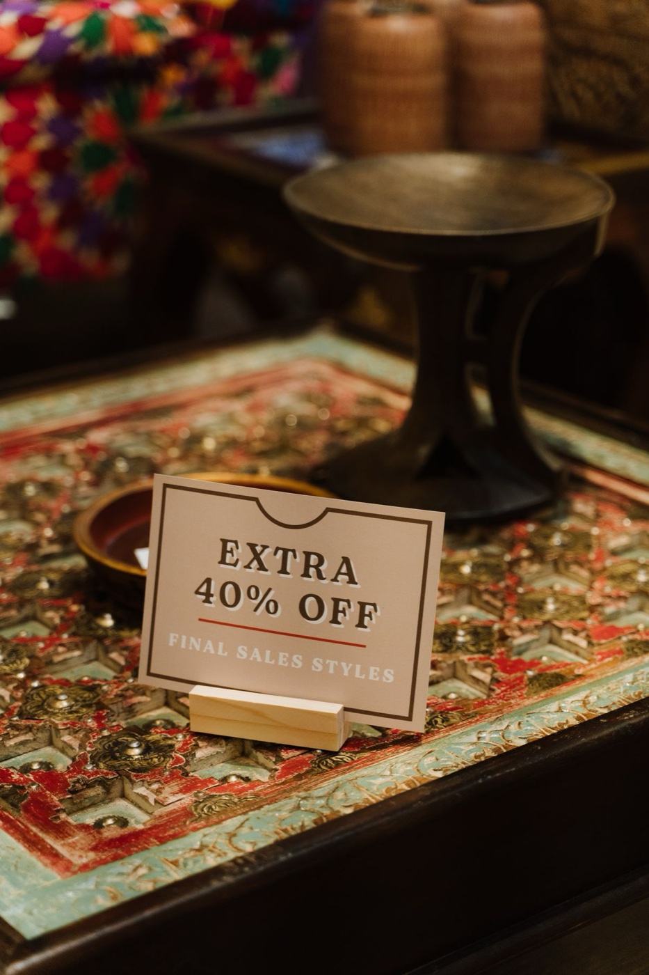 A printed sign reading extra 40 percent off final sales styles standing on a carved wooden table in a shop