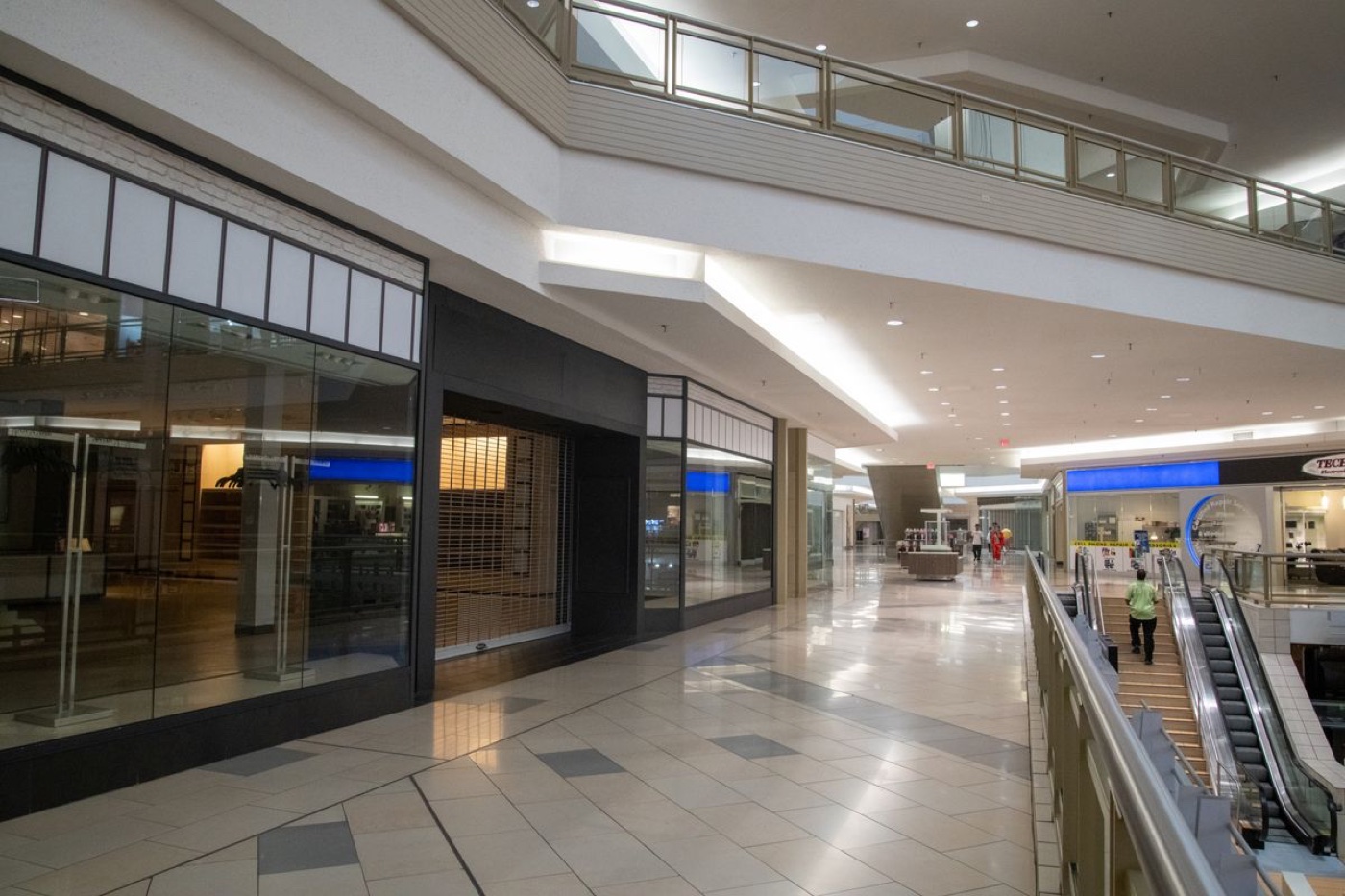 An indoor shopping mall corridor with a shuttered storefront behind dark gates next to an escalator