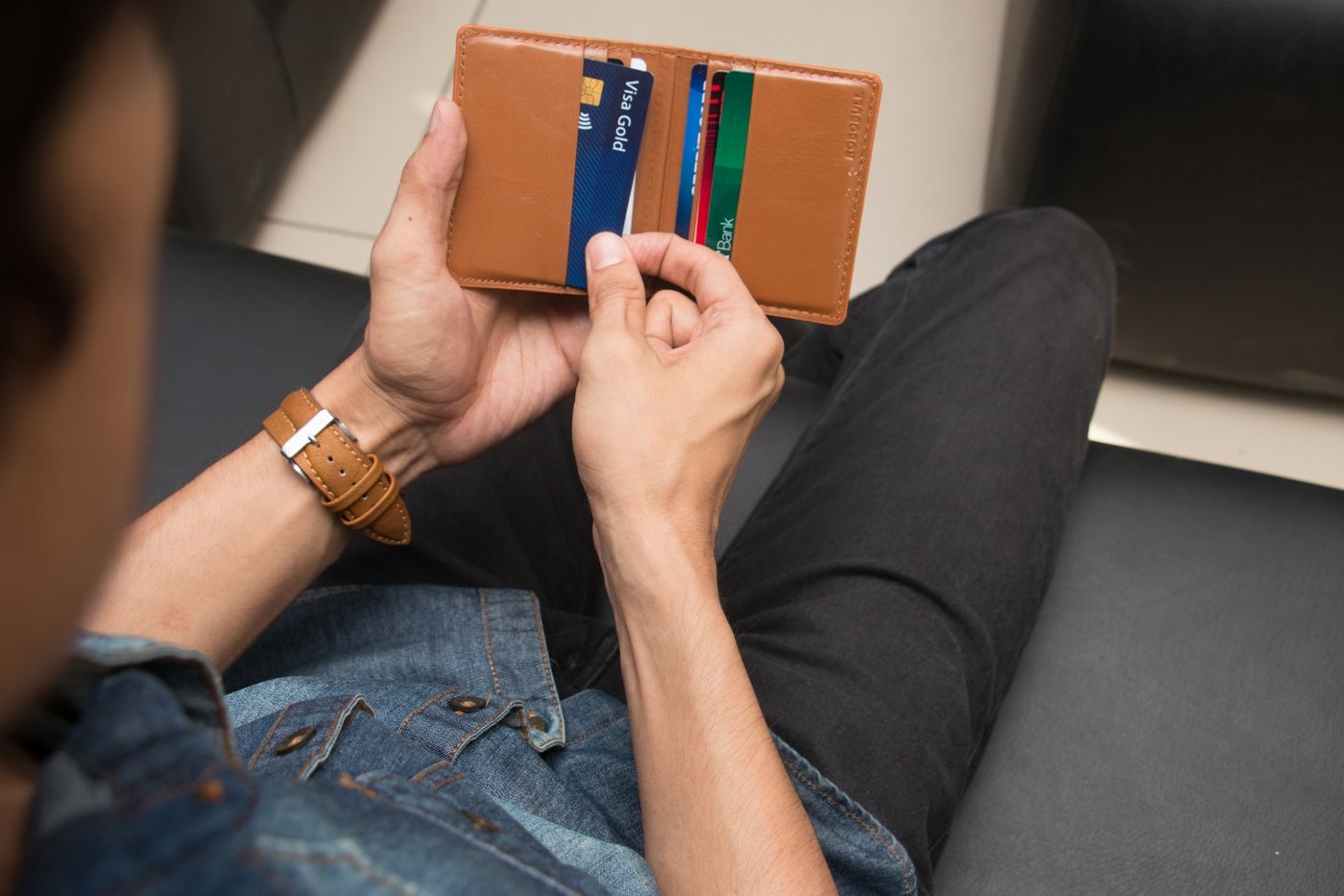 Hands holding an open tan leather wallet with several payment cards slotted inside, seen from above