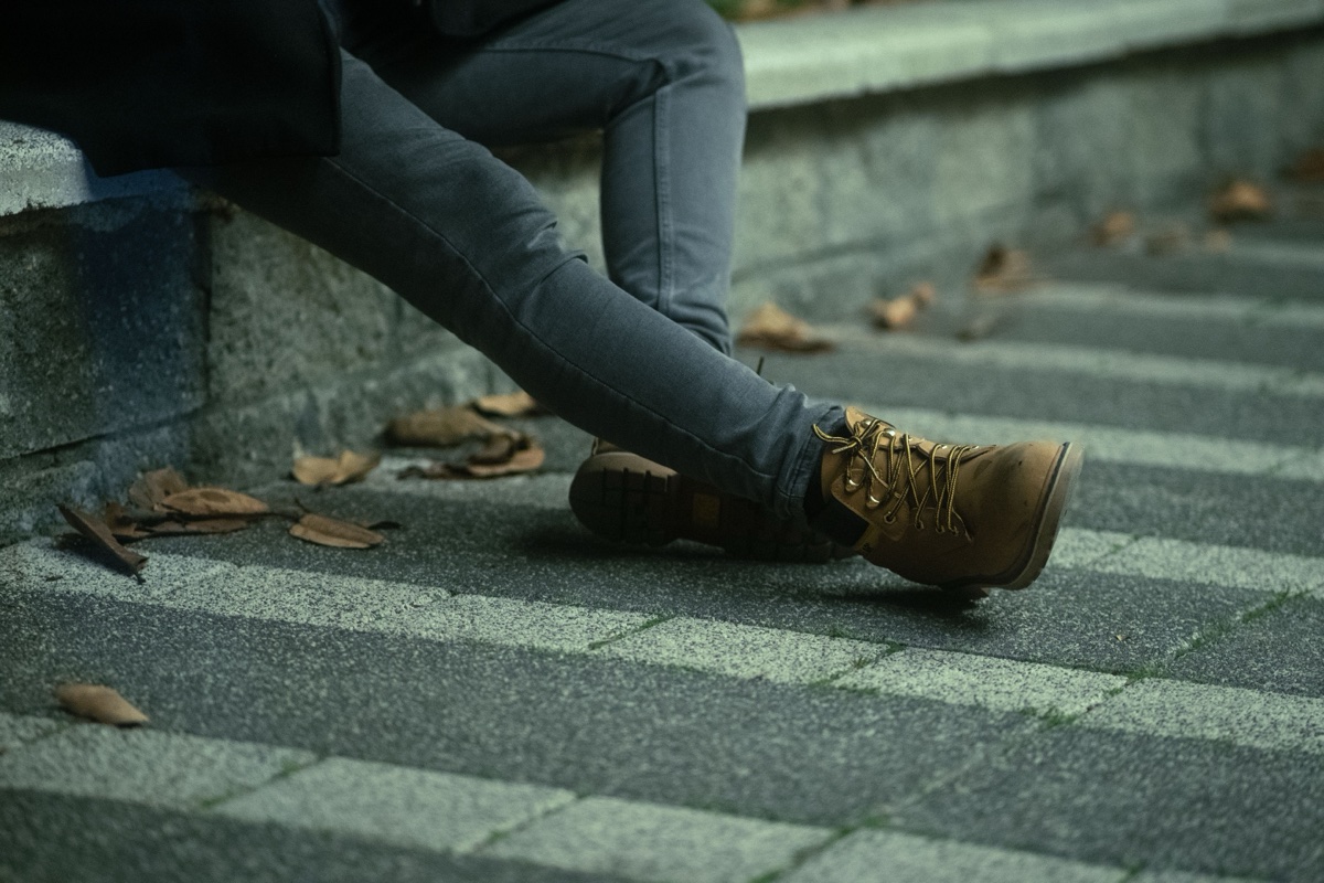 A man's legs in slim grey stretch jeans and tan work boots, stretched out across stone steps