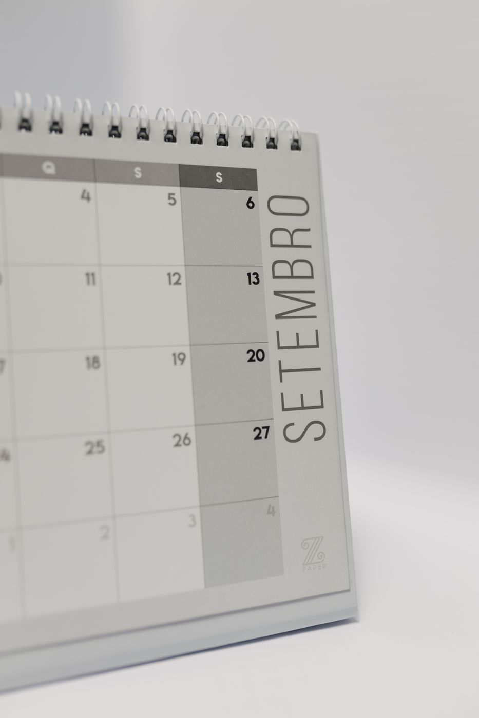 A grey spiral desk calendar open to a September page, with the final weekend column shaded and the Saturday dates printed in bold