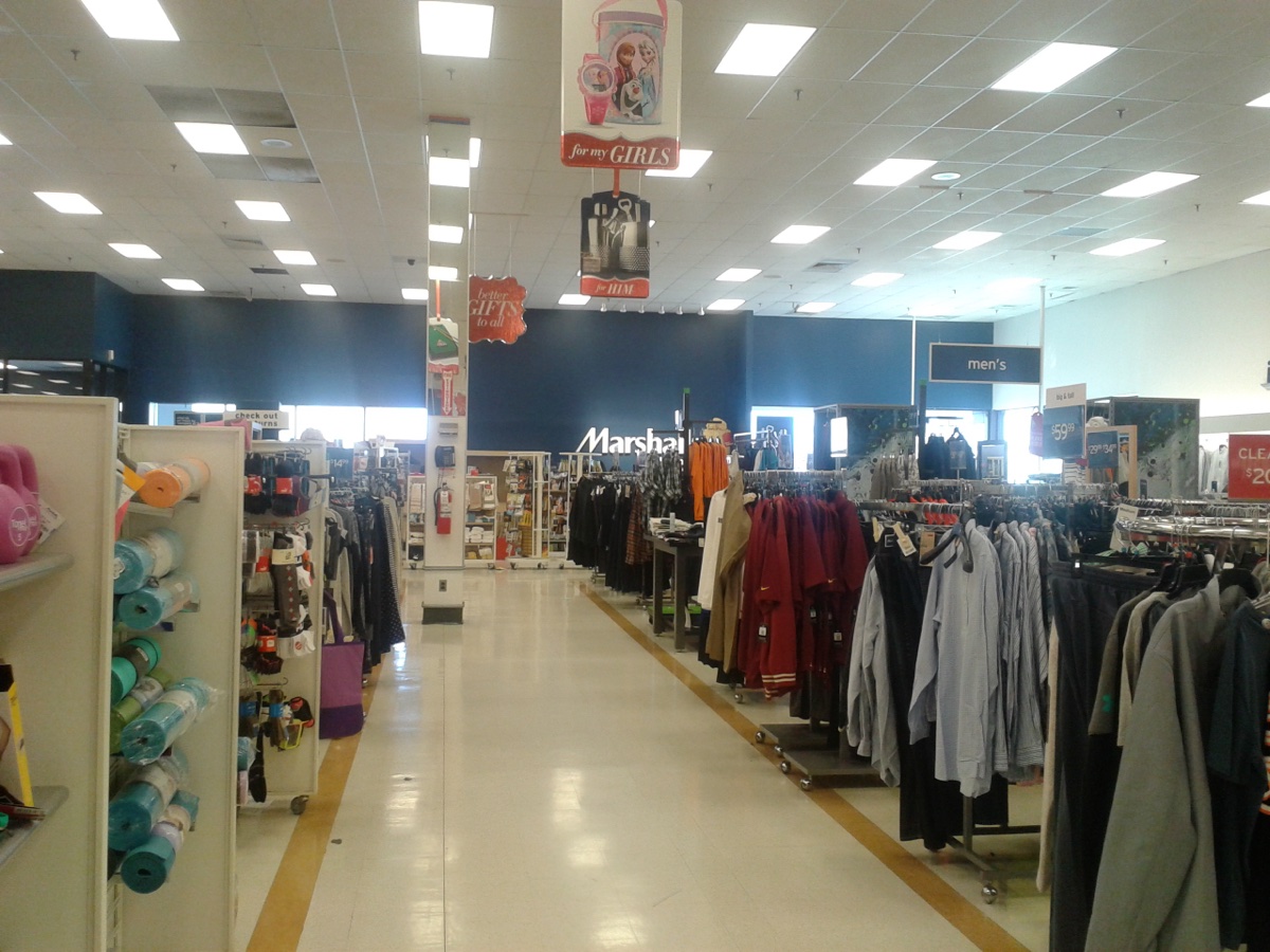 Center aisle of a Marshalls store with men's shirt racks on the right and a returns sign visible near the registers