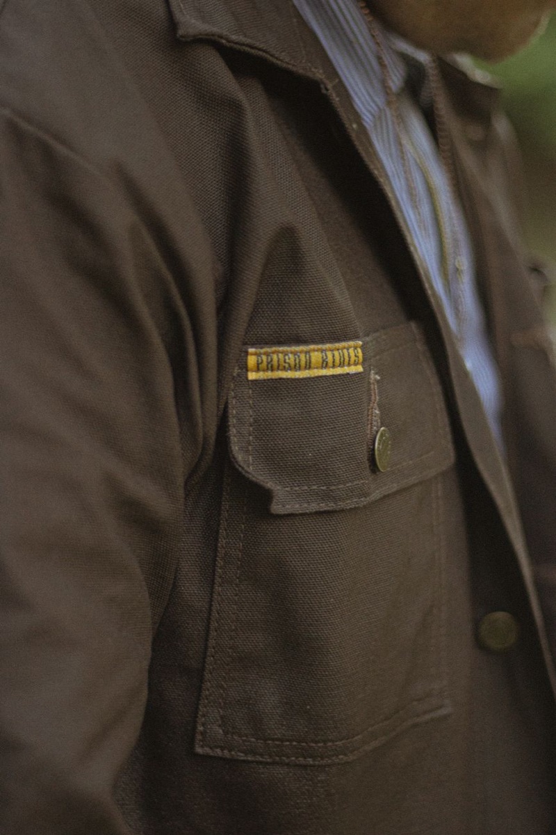 Close-up of a dark brown canvas work jacket showing a buttoned chest pocket flap and heavy stitching
