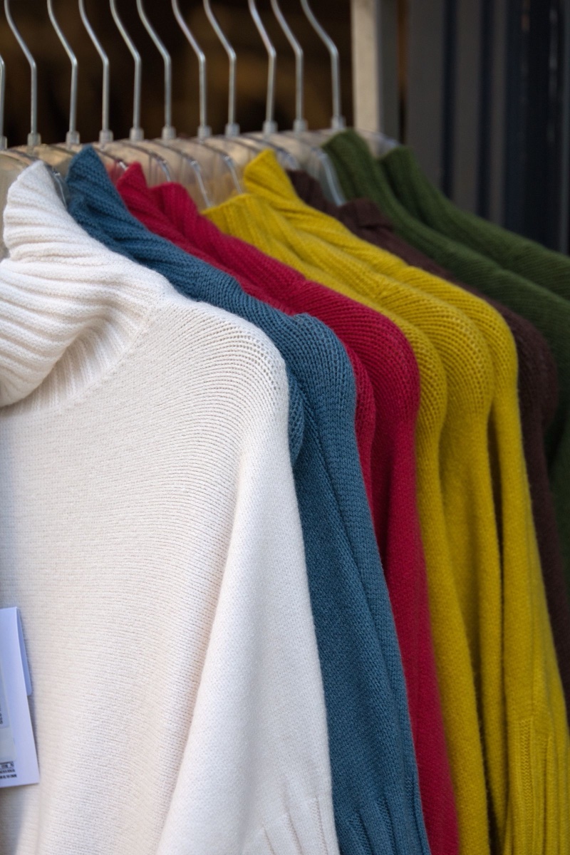 A rail of fine-gauge knit jumpers in cream, teal, red, mustard, burgundy and green, a paper price ticket visible on the first one
