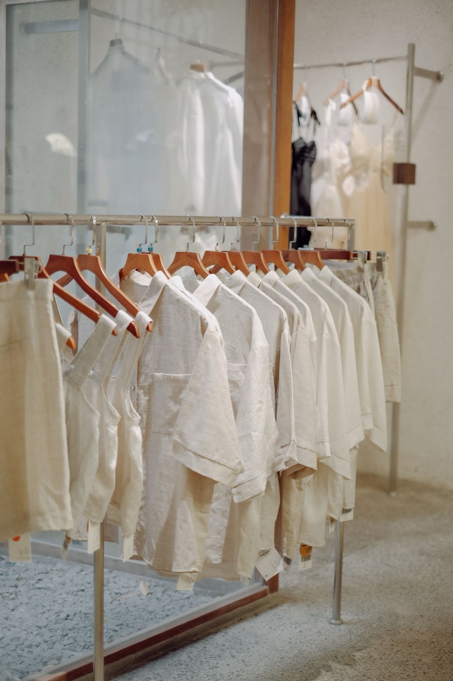 A rail of oatmeal and cream linen shirts on wooden hangers with paper price tags, shot in daylight