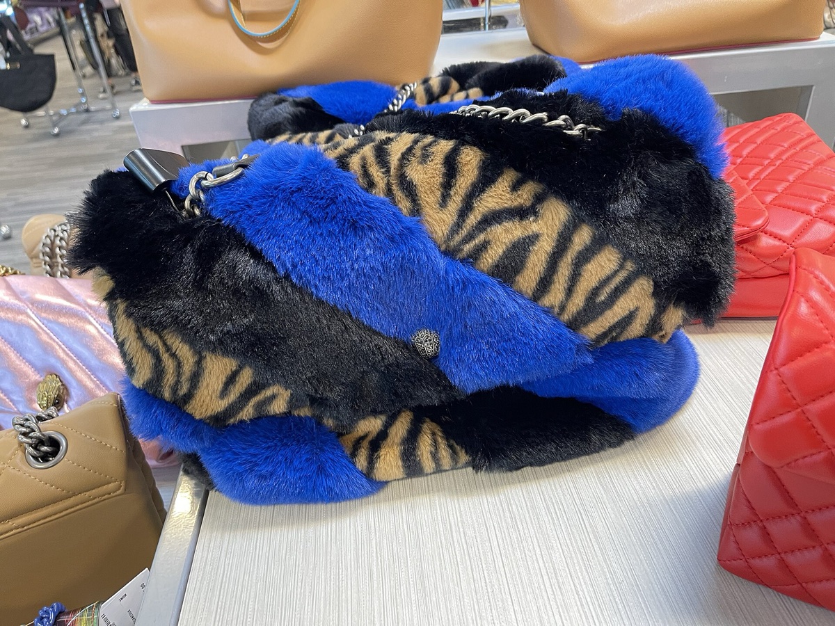 Handbags piled on a table at Nordstrom Rack: a black and blue faux-fur bag with tiger-print panels, a red quilted bag, a tan leather one behind