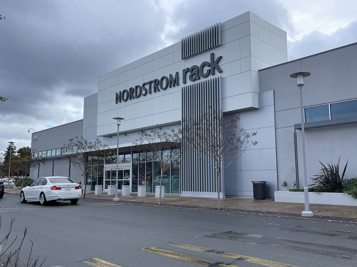 Grey Nordstrom Rack storefront under an overcast sky, a white car in the parking lot outside