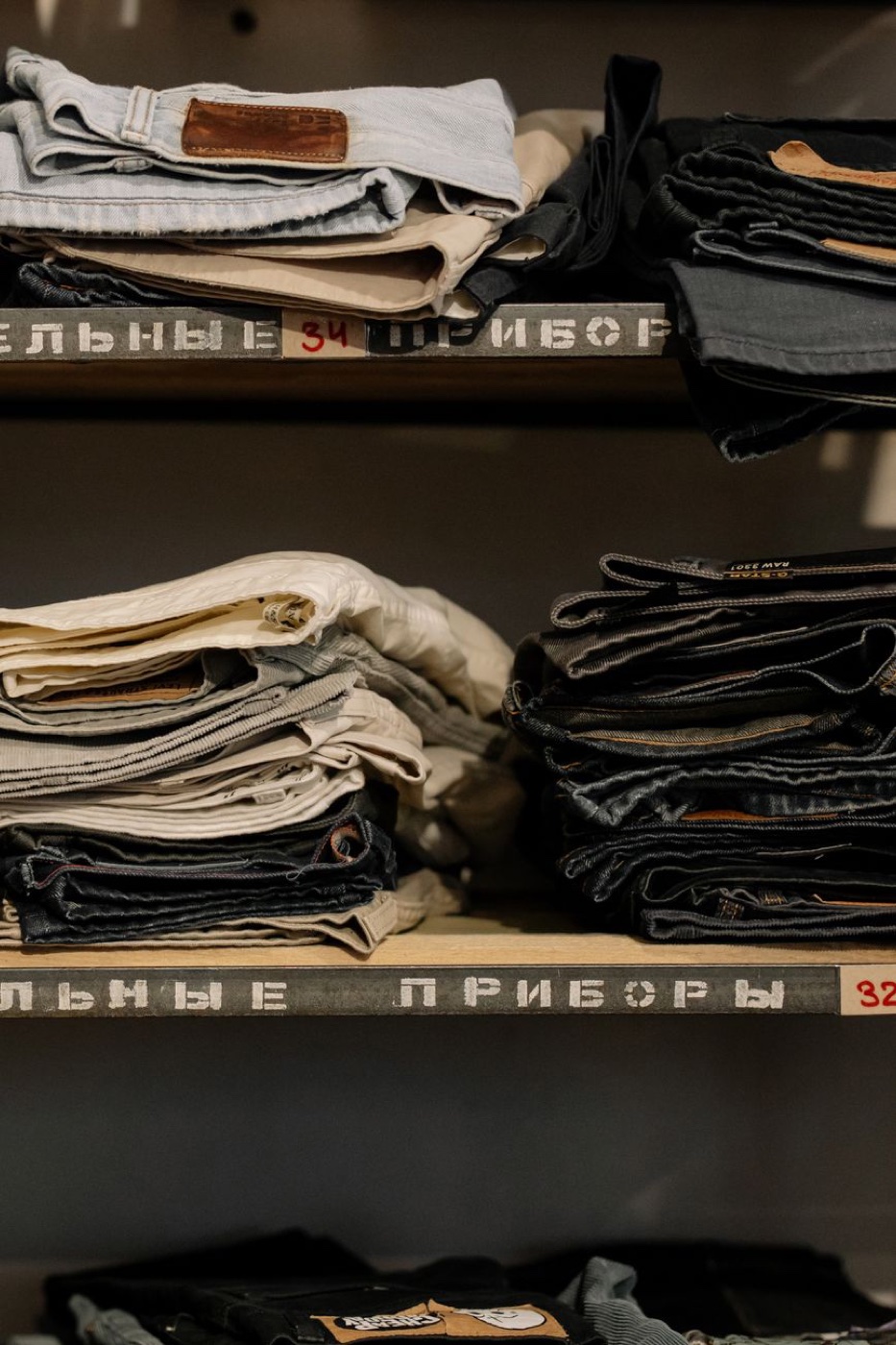 Shelves of folded jeans and corduroy trousers in a secondhand shop, with waist sizes stencilled on the shelf edges