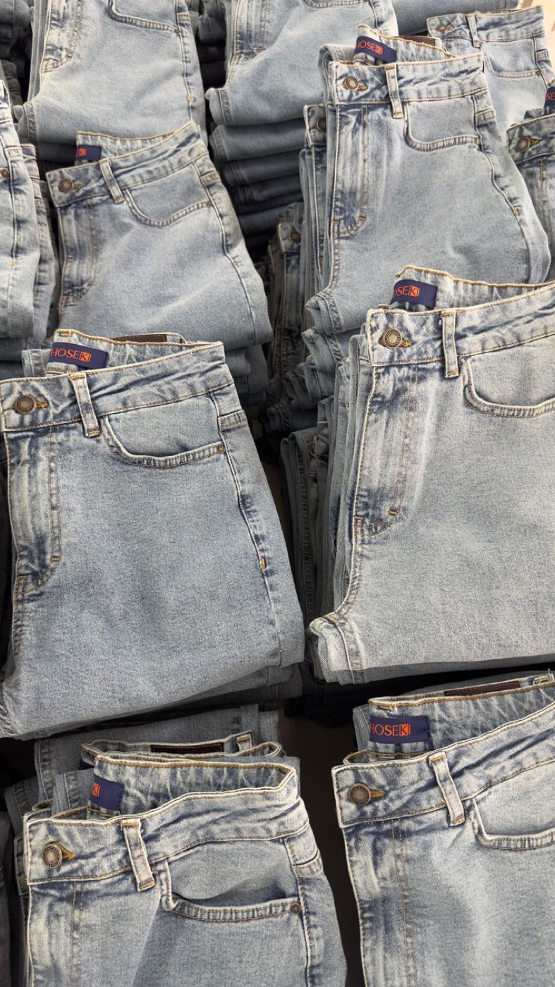 Dozens of pairs of light-wash jeans folded and stacked on a retail table, brand tabs visible at the waistbands