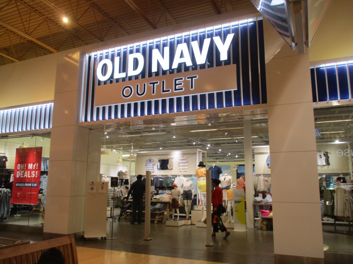 Illuminated Old Navy Outlet sign over a mall storefront, with an Oh My Deals banner in the window and mannequins inside