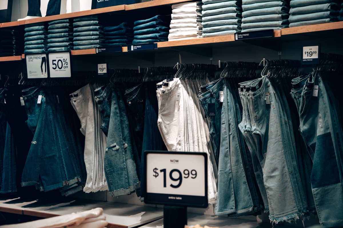 Wall of hanging jeans in a clothing store under shelves of folded denim, with a 50% off sign and a $19.99 price card