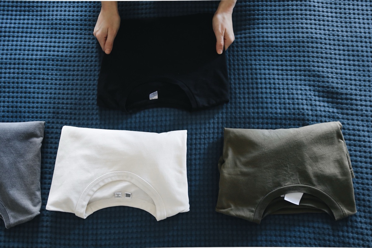 Hands laying out four folded t-shirts in black, white, olive and grey on a blue waffle-knit blanket