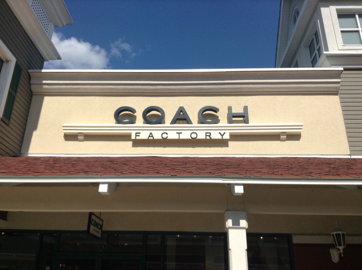 Coach Factory storefront sign in an outlet center on a sunny afternoon