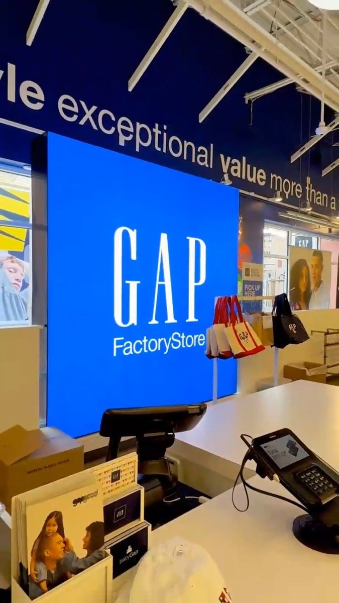 Gap Factory Store register with a lit blue logo panel and the words exceptional value painted along the ceiling beam above it