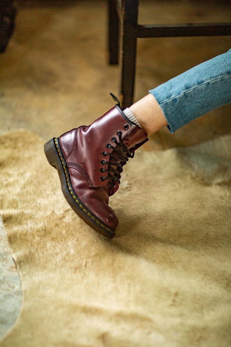 Close-up of a laced oxblood leather combat boot worn with light-wash jeans over a tan cowhide rug