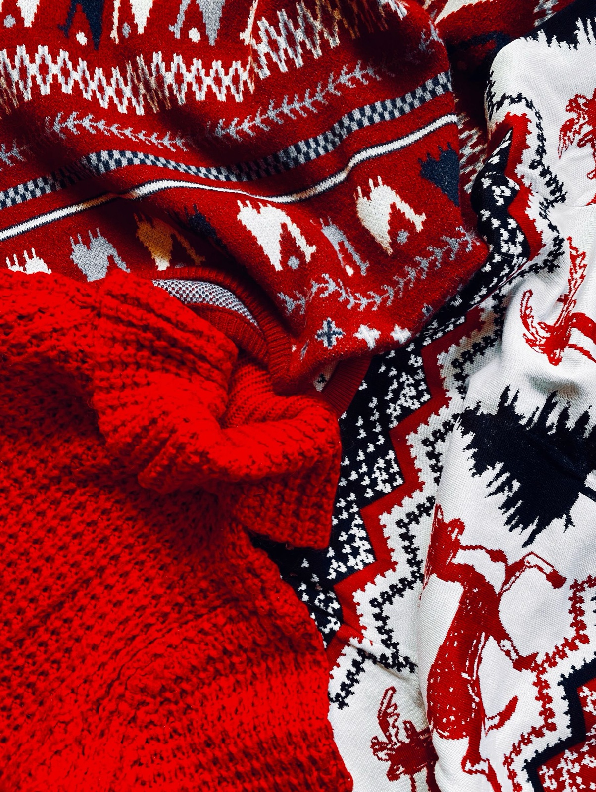 A heap of red, navy and cream patterned knits, several worked with deer and animal motifs