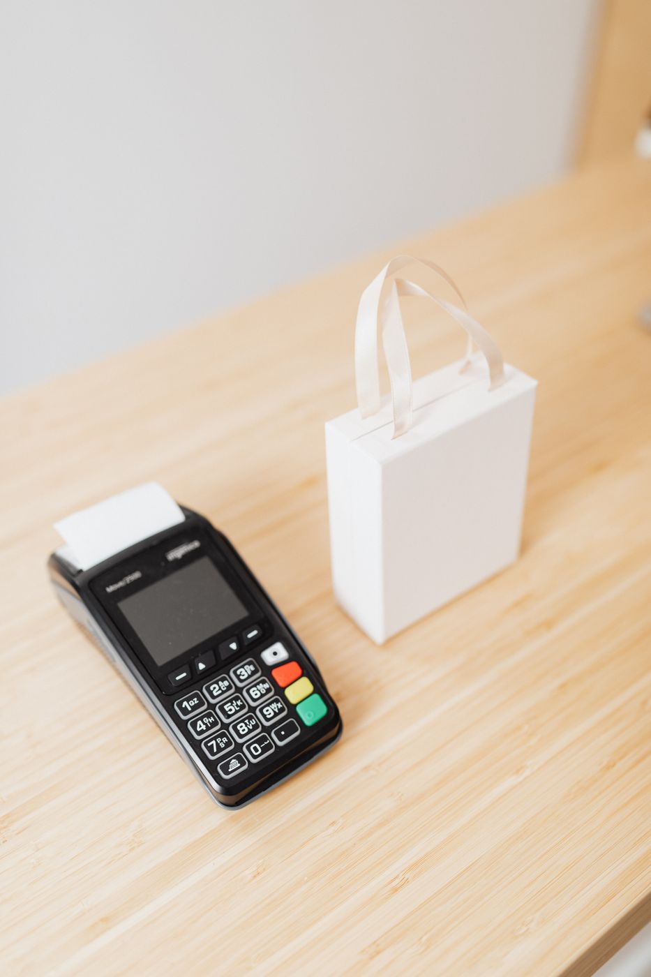 A card payment terminal beside a small white gift bag on a wooden store counter