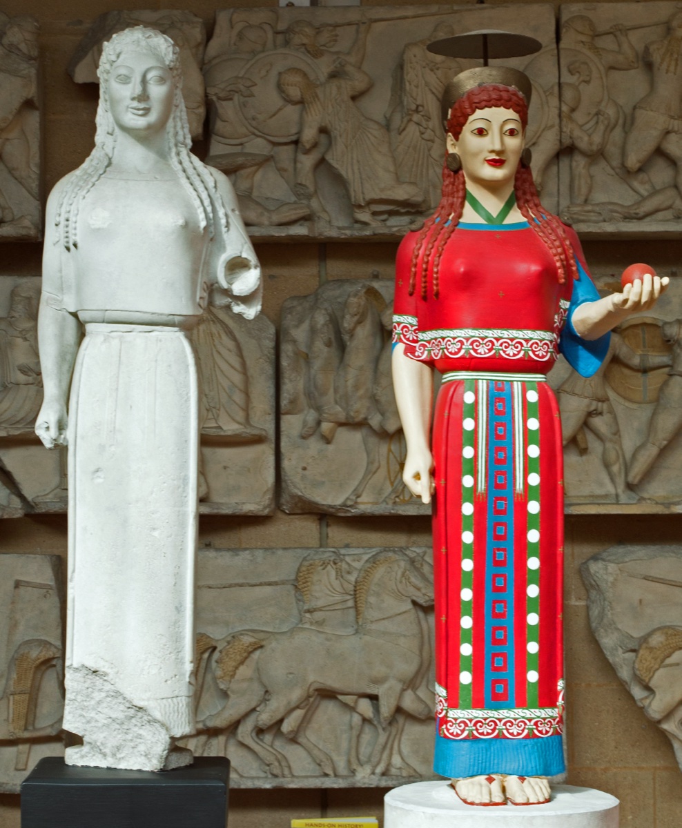 A plain plaster cast of the Peplos Kore statue standing beside a brightly painted reconstruction of the same figure in red and blue at the Museum of Classical Archaeology, Cambridge