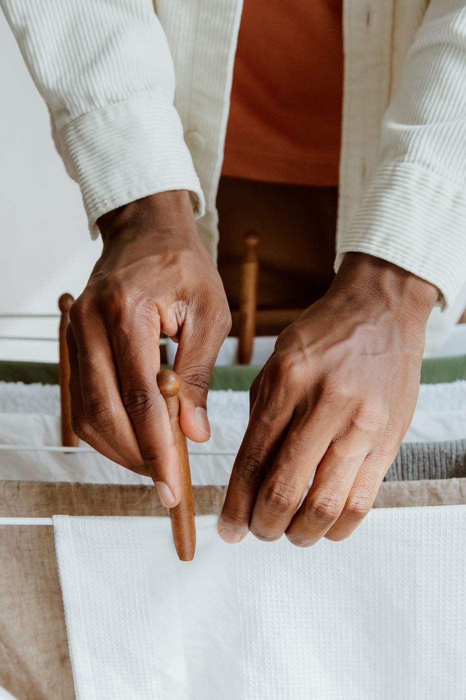 Close-up of hands pinning a white waffle-weave cloth to an indoor drying line with a wooden clothespin