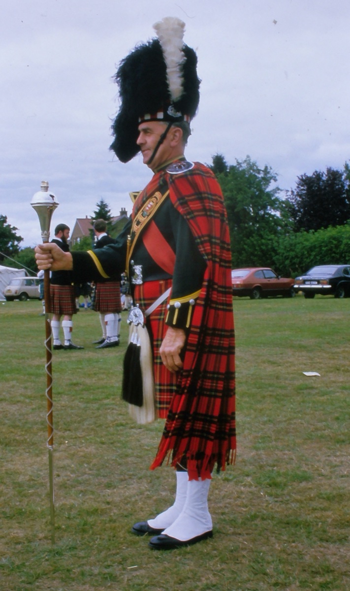 A drum major at the Stirling Highland Games in April 1984, in full dress uniform with a red tartan plaid draped over his left shoulder