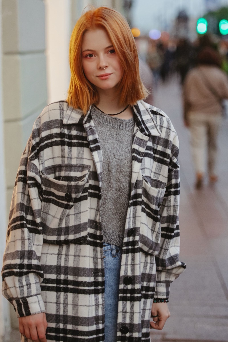 A black and white plaid overshirt worn open over a gray knit top on a city sidewalk at dusk
