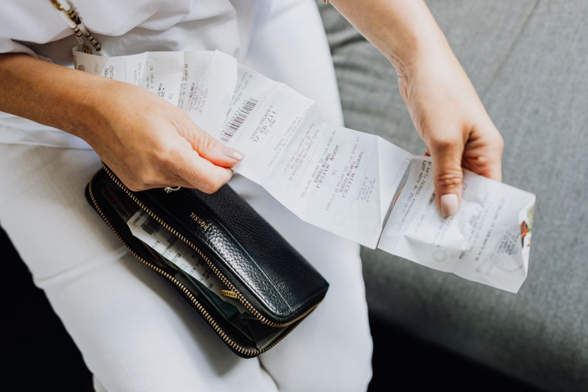 Two hands sorting a fan of long paper receipts over a black wallet