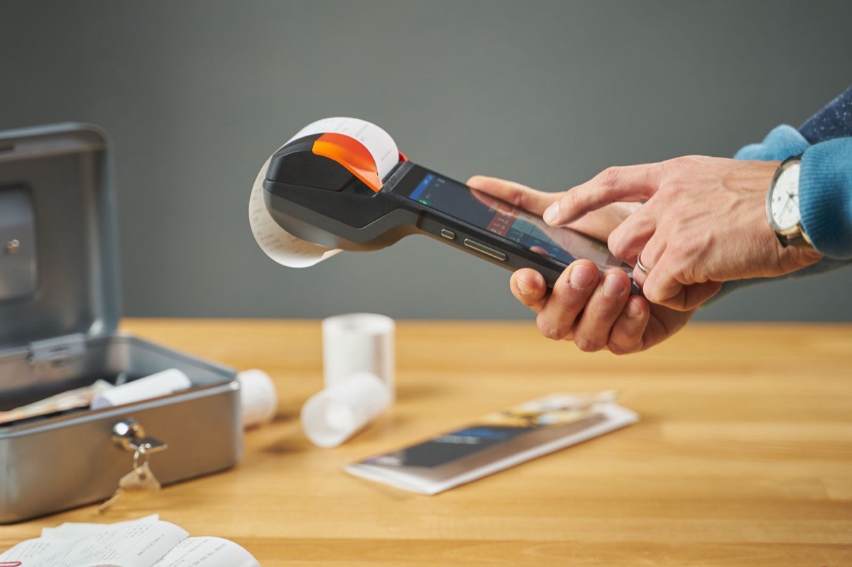 Hands holding a payment terminal as it prints a paper receipt over a wooden counter