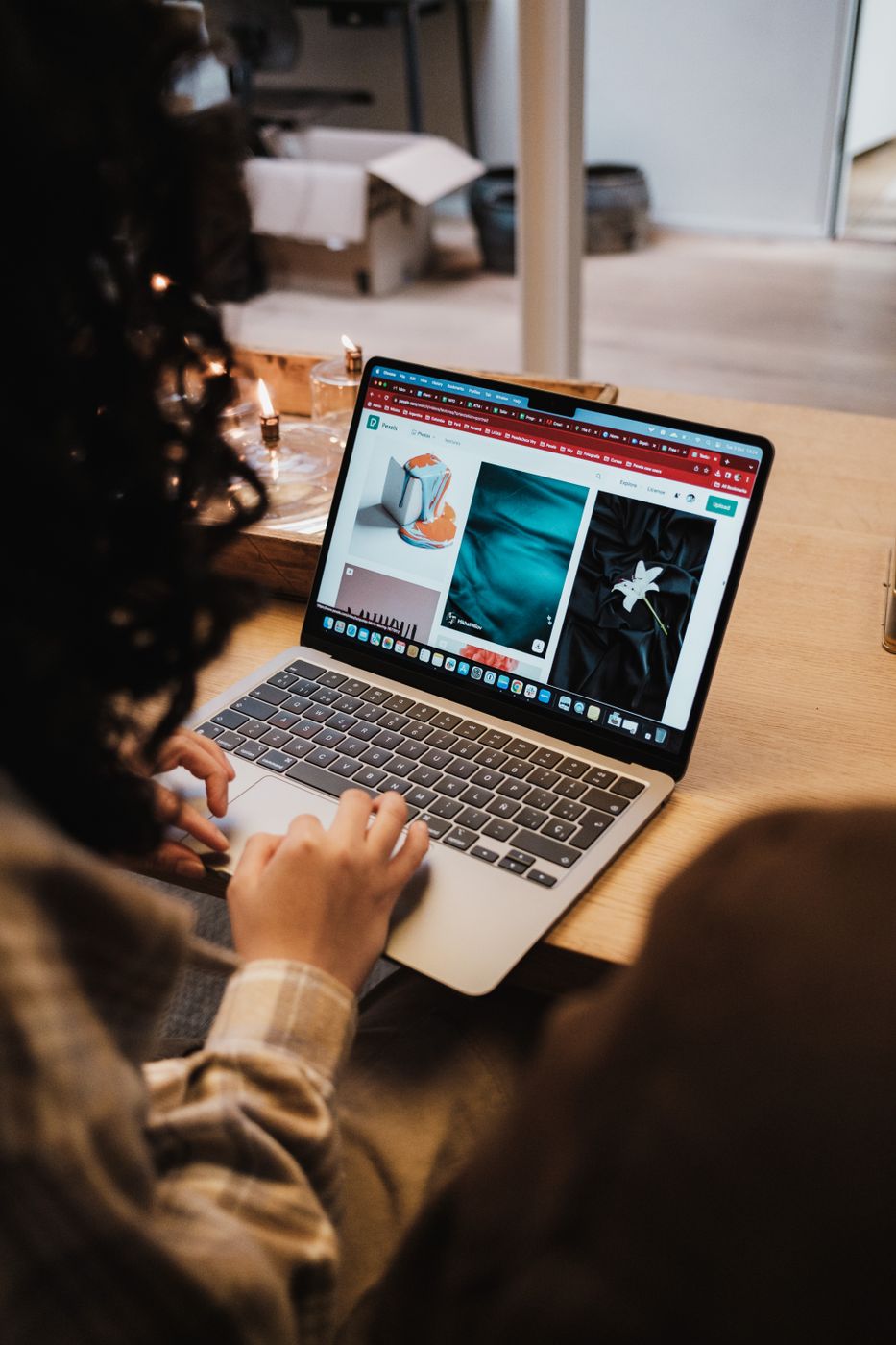 Over the shoulder view of a person at a wooden table scrolling a clothing shop on a laptop, with an open cardboard box behind them