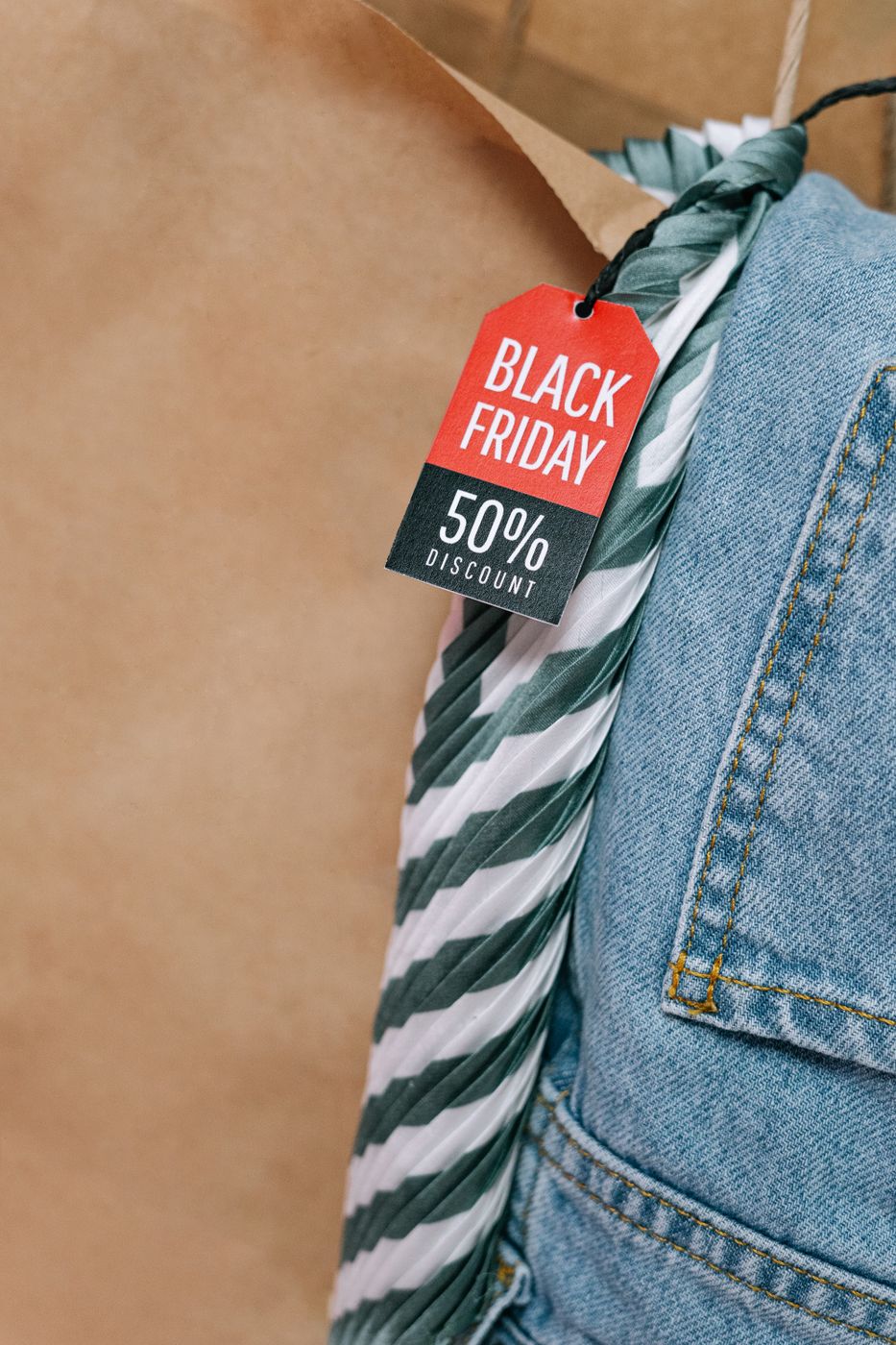 A red and black Black Friday tag reading 50% discount, hanging by a string against denim and a striped garment