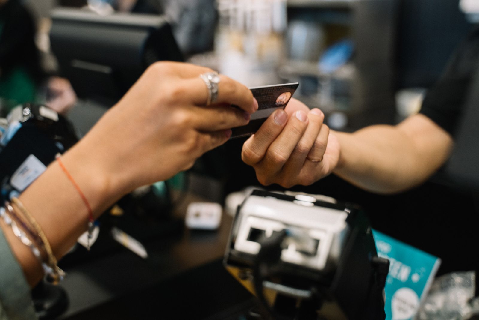 Two pairs of hands passing a bank card over a store counter beside a card terminal