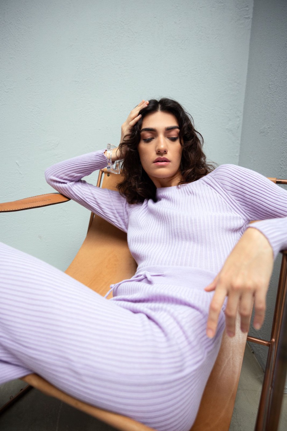 Woman reclining in a leather sling chair wearing a matching lilac ribbed knit top and pants