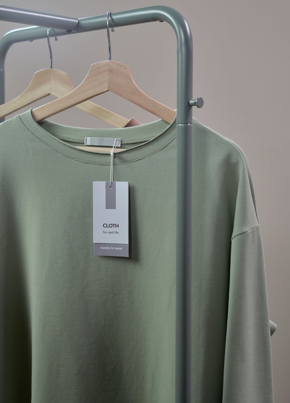 A sage green top on a wooden hanger with a white hang tag reading ready to wear clipped at the collar