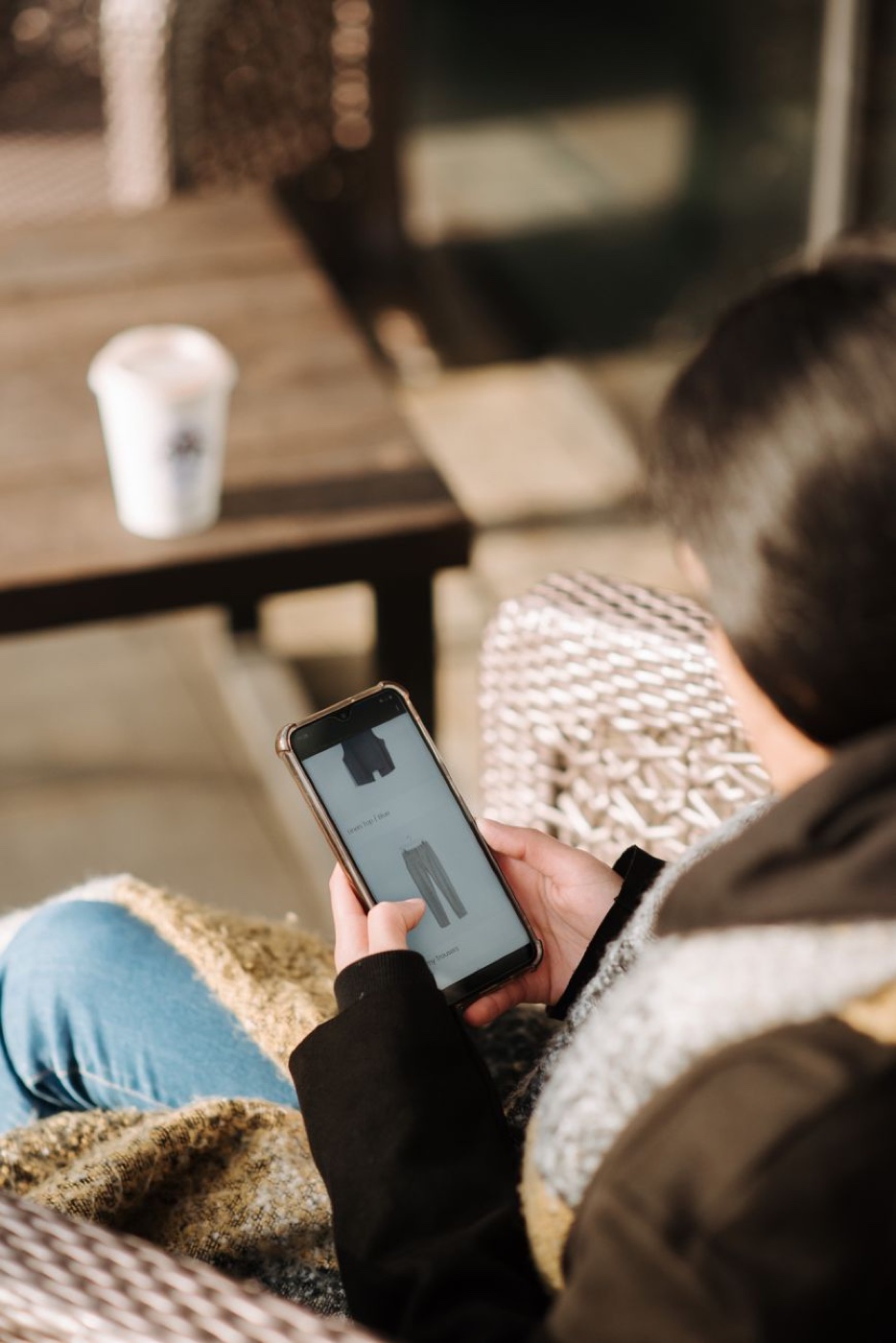 Over-the-shoulder view of a person browsing a clothing resale listing on a smartphone outdoors