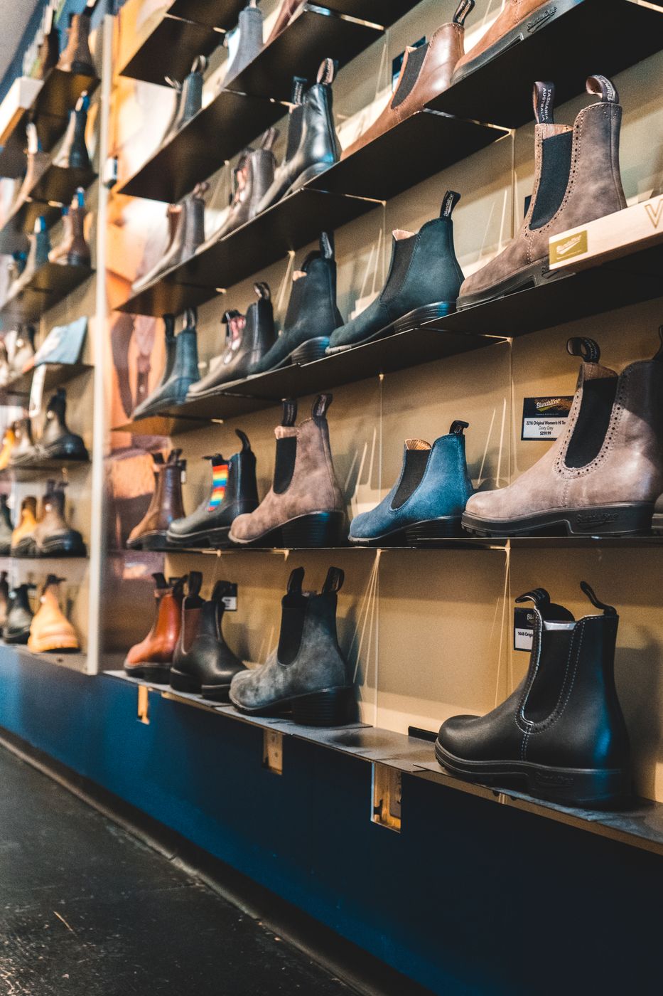 A tall wall of shelves in a footwear store filled with suede and leather chelsea boots in brown, blue and black